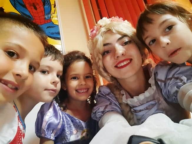 Selfie de grup cu o animatoare în costum de prințesă și copii; fotografia arată interacțiunea de aproape.